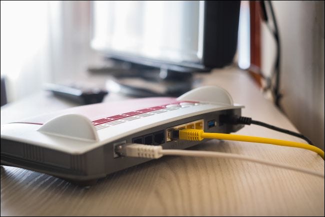 Câbles branchés à l'arrière d'un modem posé sur un bureau à côté d'un ordinateur.