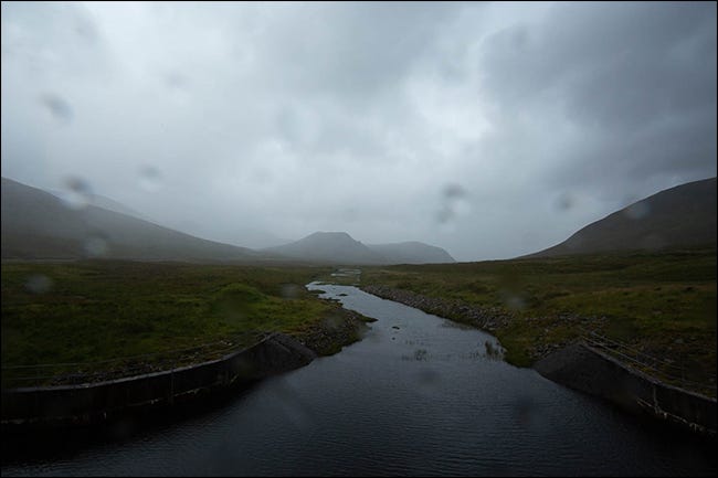 Une photo pluvieuse d'une montagne et d'un ruisseau avec des gouttelettes d'eau sur l'objectif. 