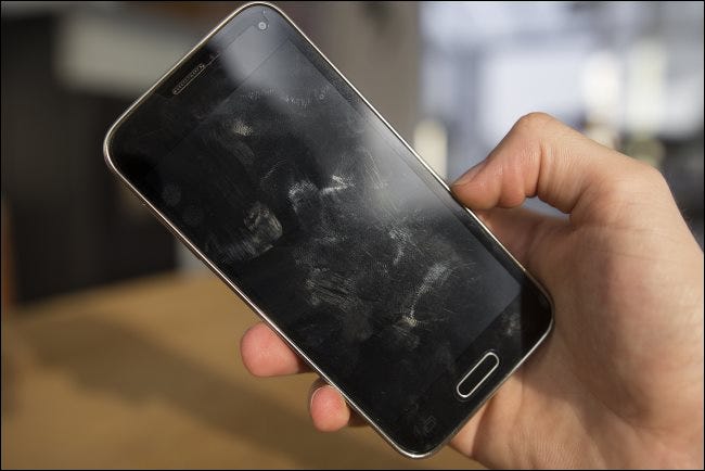 Une main tenant un téléphone Android avec des taches sur l'écran.