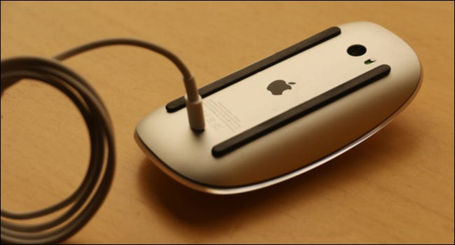 Une souris Apple à l'envers avec le câble de charge attaché.
