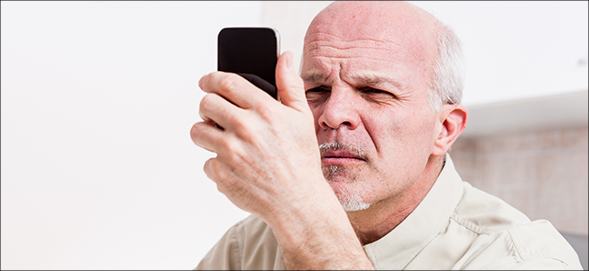 Un homme regarde son téléphone, endurant clairement une sérieuse fatigue oculaire.